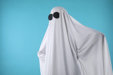 Creepy ghost. Person covered with white sheet on light blue background, space for text