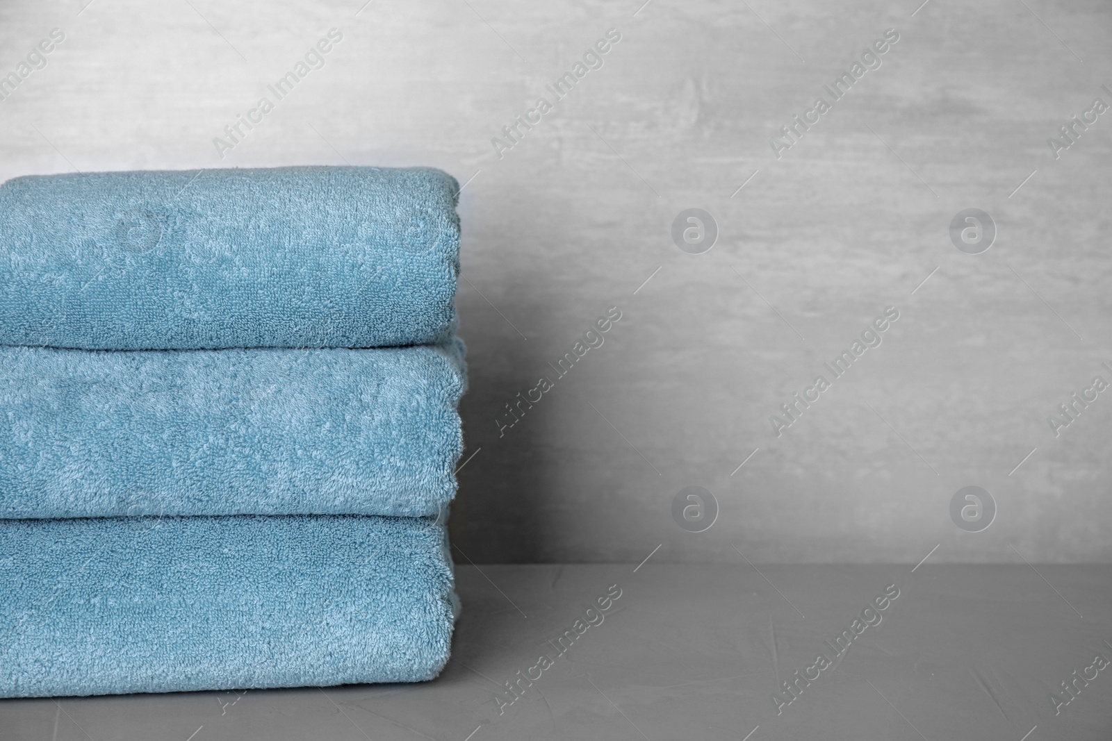 Photo of Stack of clean bath towels on grey table. Space for text