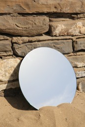 Round mirror reflecting sky on sand near stone wall outdoors