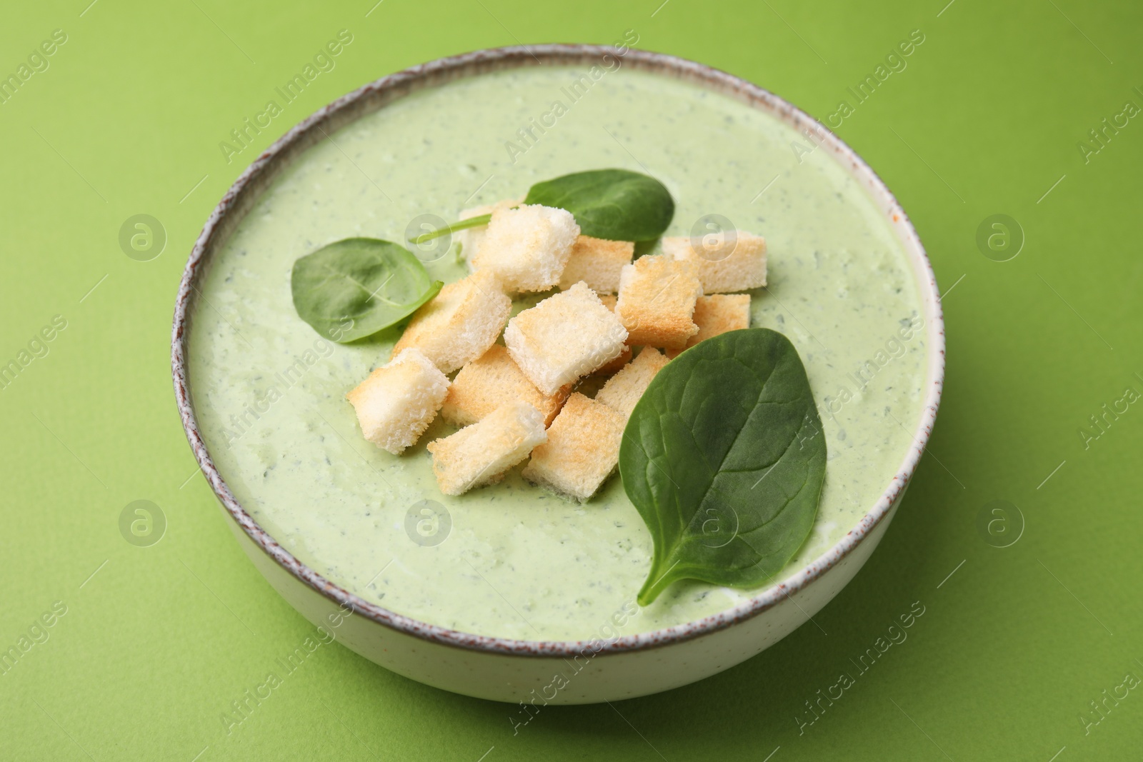 Photo of Delicious spinach cream soup with leaves and croutons in bowl on green background