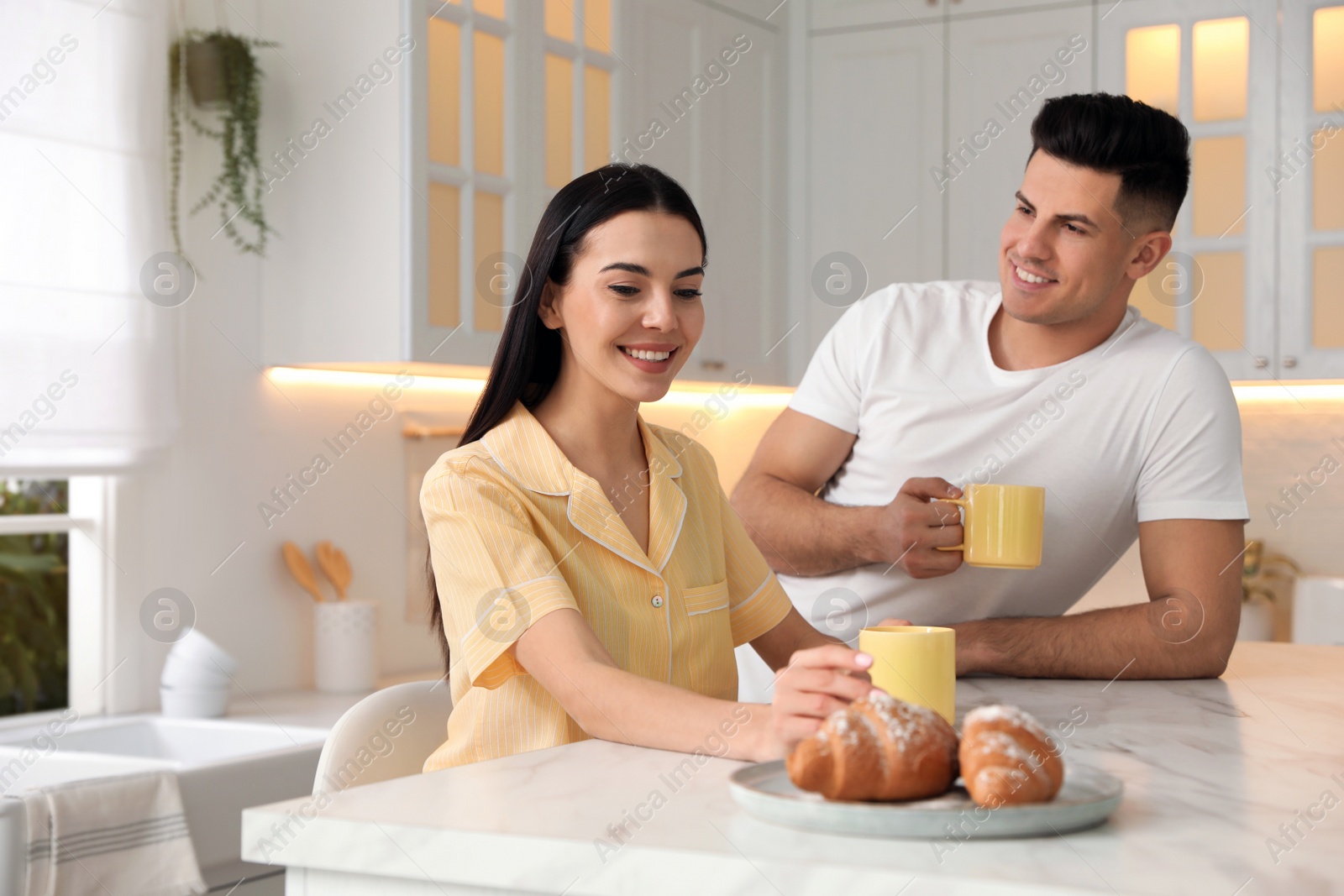 Photo of Happy couple wearing pyjamas during breakfast at table in kitchen