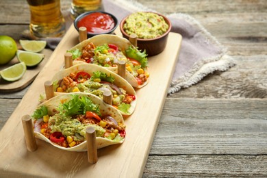 Delicious tacos with guacamole, meat and vegetables served on wooden table. Space for text