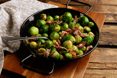 Photo of Delicious Brussels sprouts with bacon on wooden table