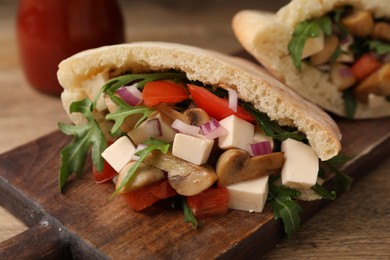 Delicious pita sandwiches with cheese, mushrooms, tomatoes and arugula on wooden table, closeup