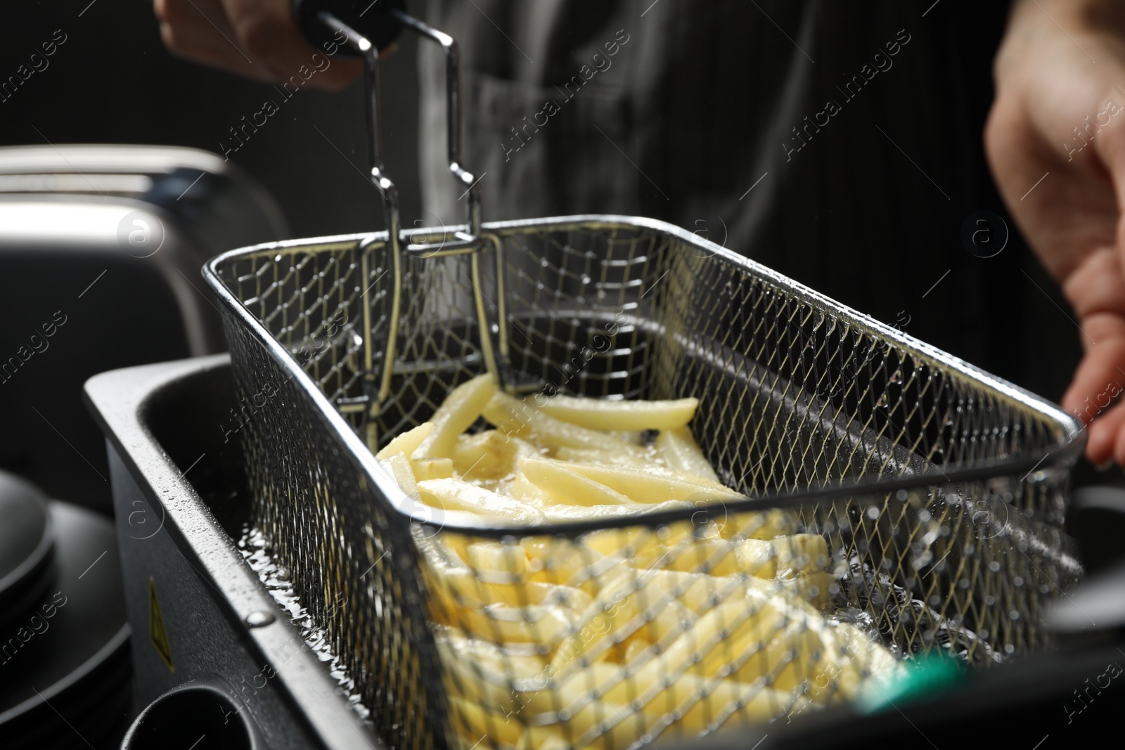 Photo of Chef cooking delicious french fries in hot oil, closeup