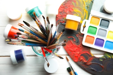 Photo of Glass jar with brushes, paints and palette on wooden background, top view