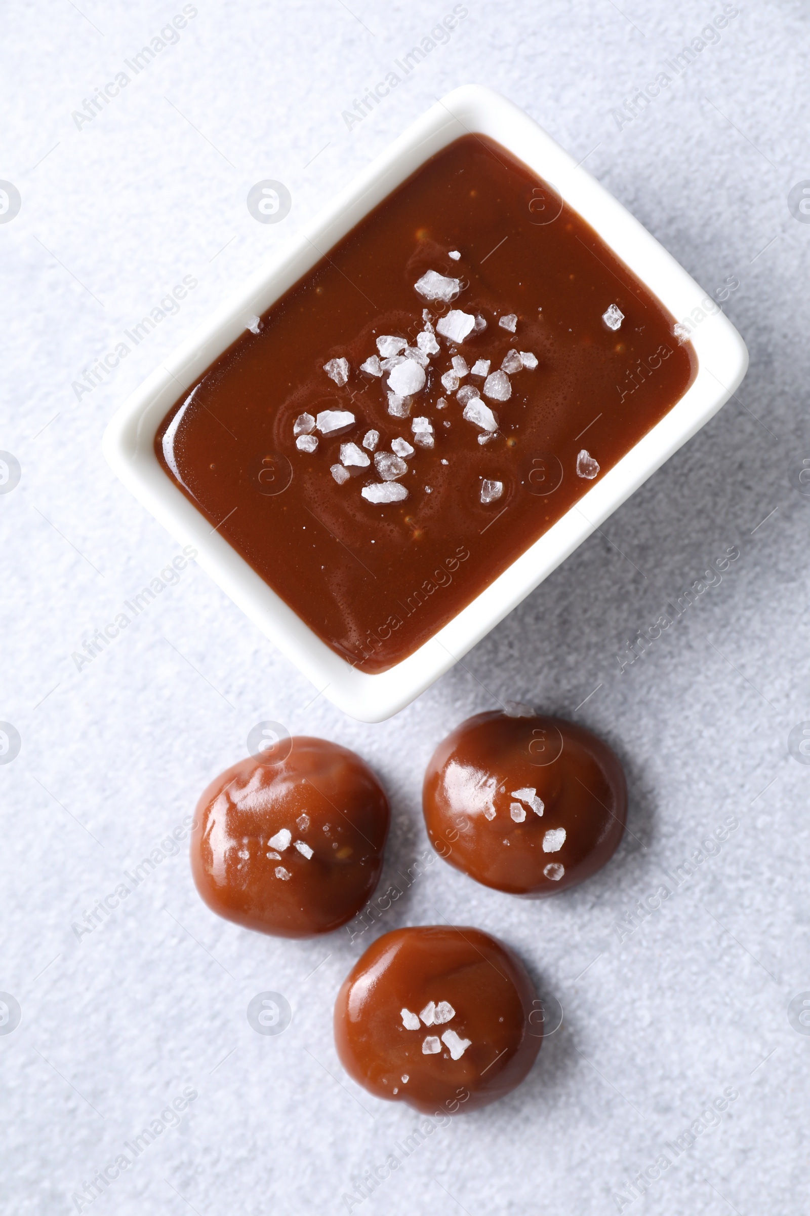 Photo of Tasty candies, caramel sauce and salt on light grey table, top view