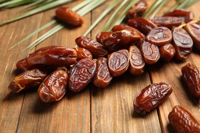 Branch with sweet dried dates and green leaf on wooden table, closeup