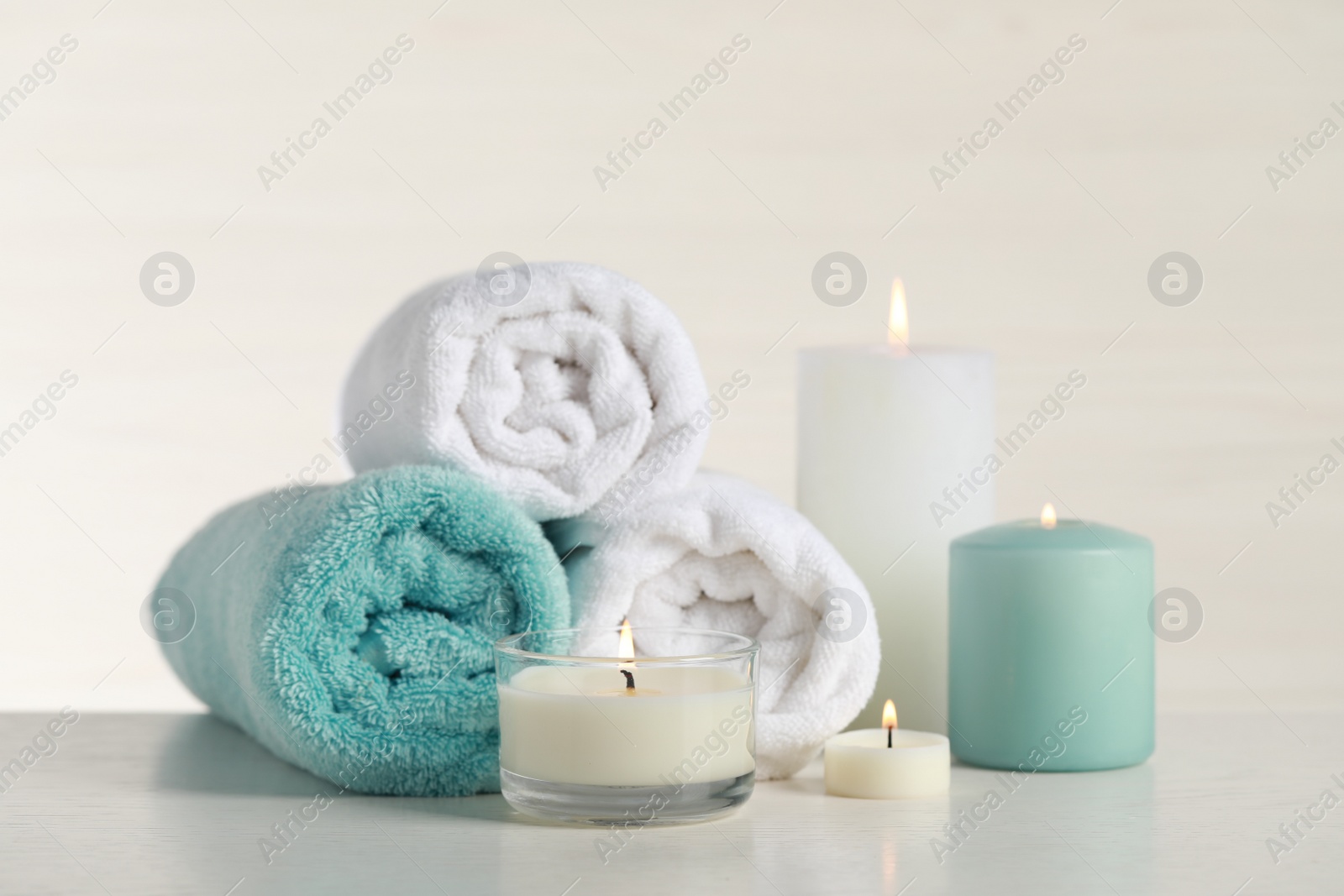 Photo of Beautiful spa composition with burning candles and rolled towels on white table