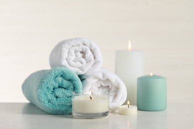 Photo of Beautiful spa composition with burning candles and rolled towels on white table