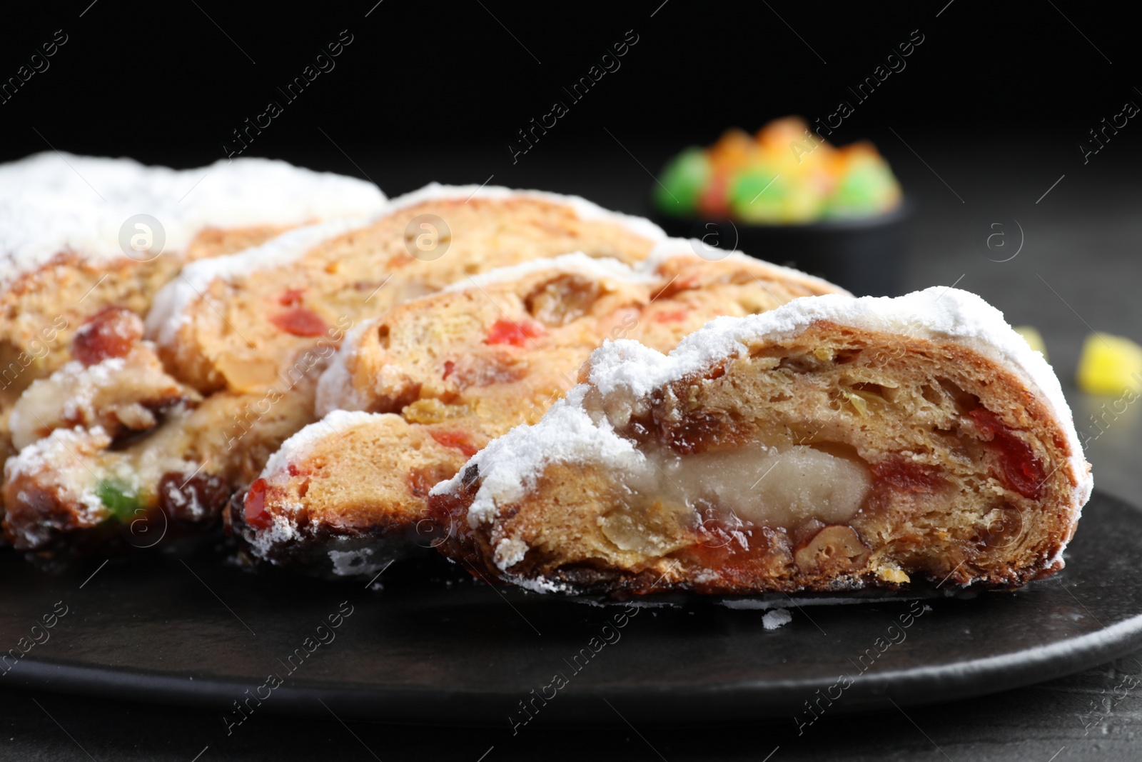 Photo of Traditional Christmas Stollen with icing sugar on black plate, closeup