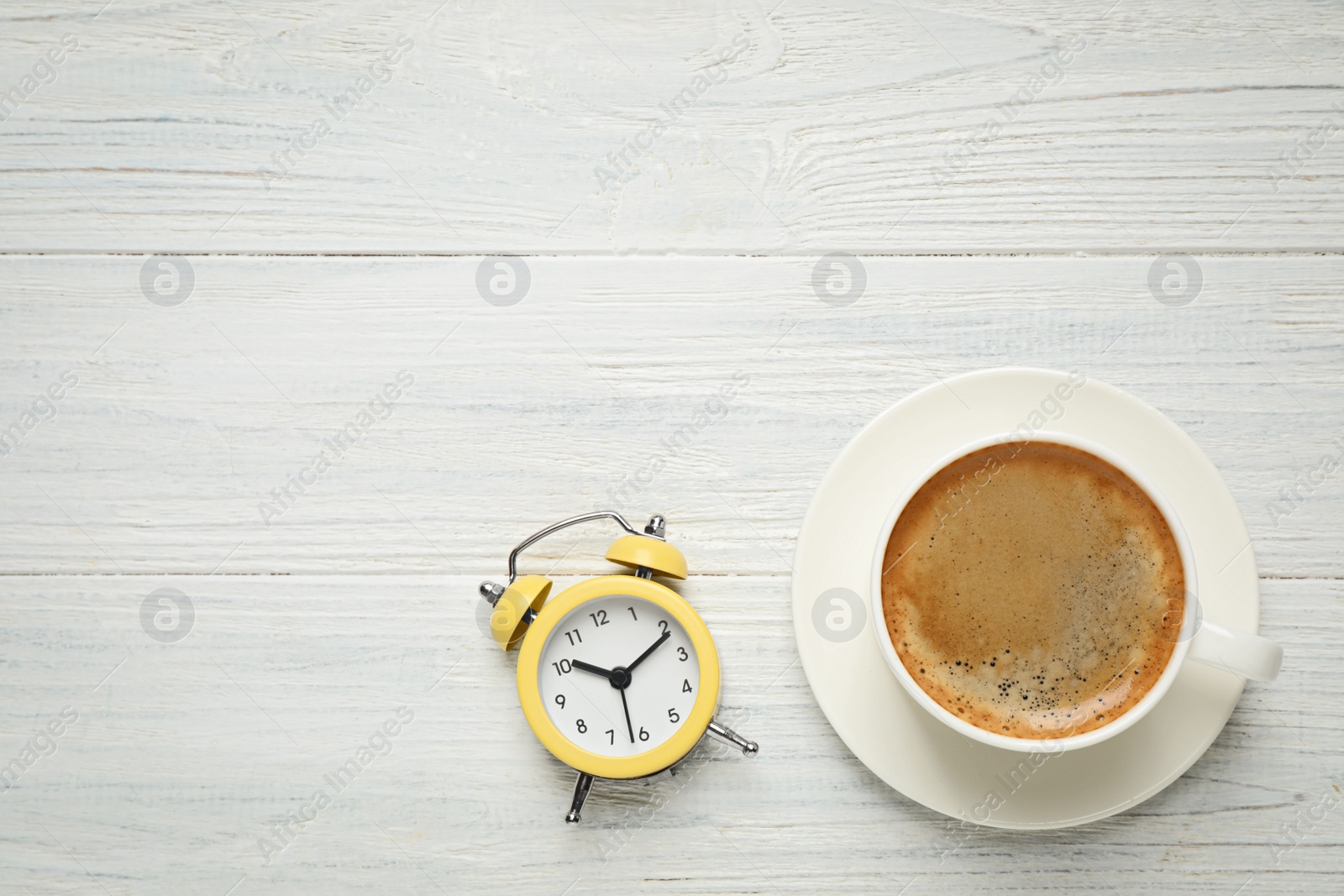 Photo of Cup of morning coffee and alarm clock on white wooden table, flat lay. Space for text