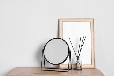 Photo of Stylish mirror, reed diffuser and picture frame on table near light wall