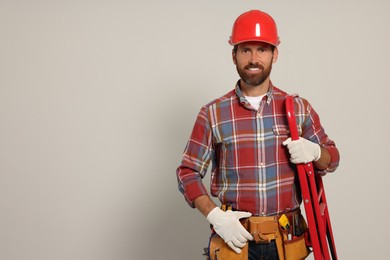 Photo of Professional builder in hard hat with tool belt and step ladder on light background, space for text
