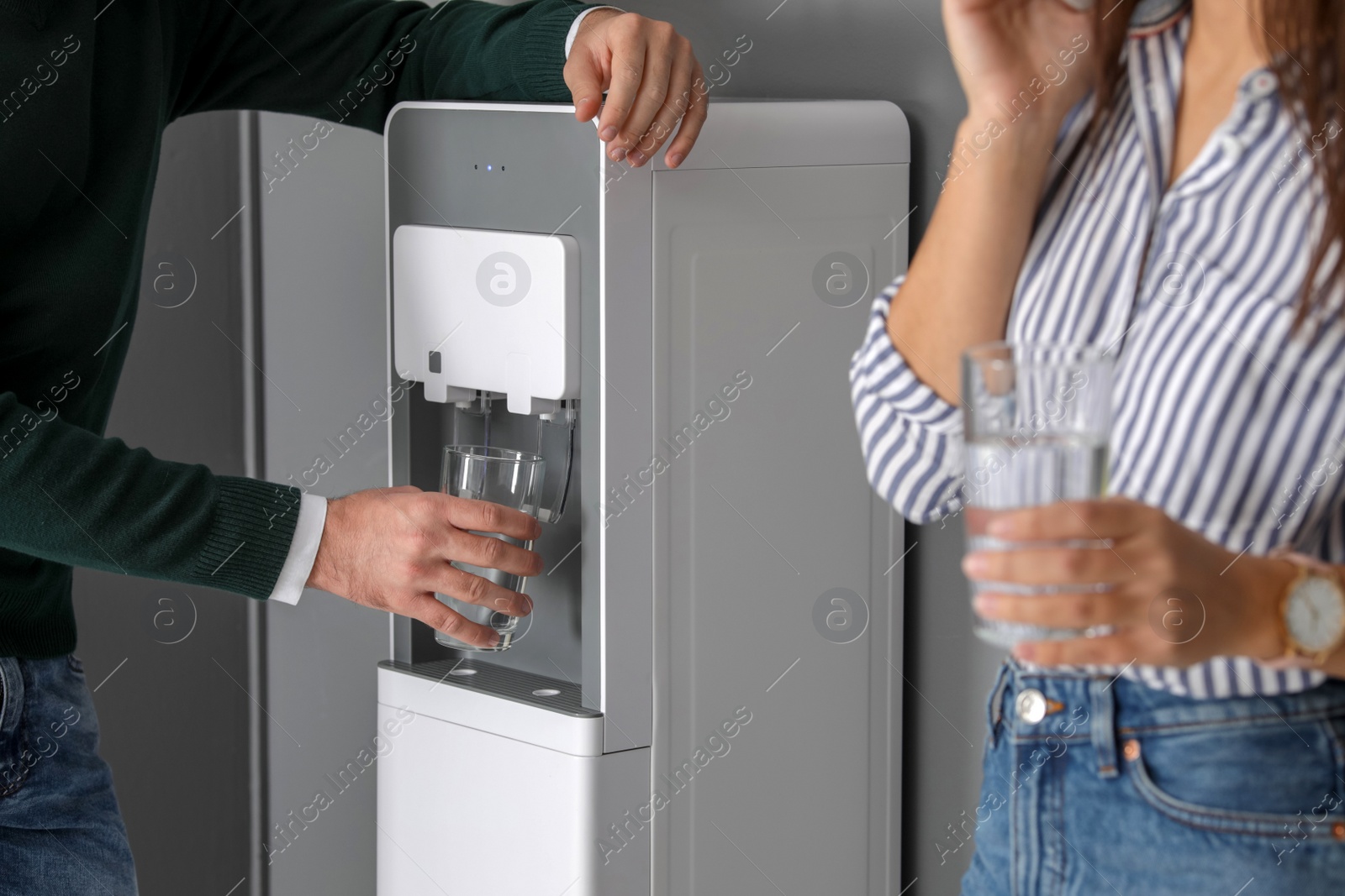 Photo of Young man taking glass of water from cooler in office, closeup