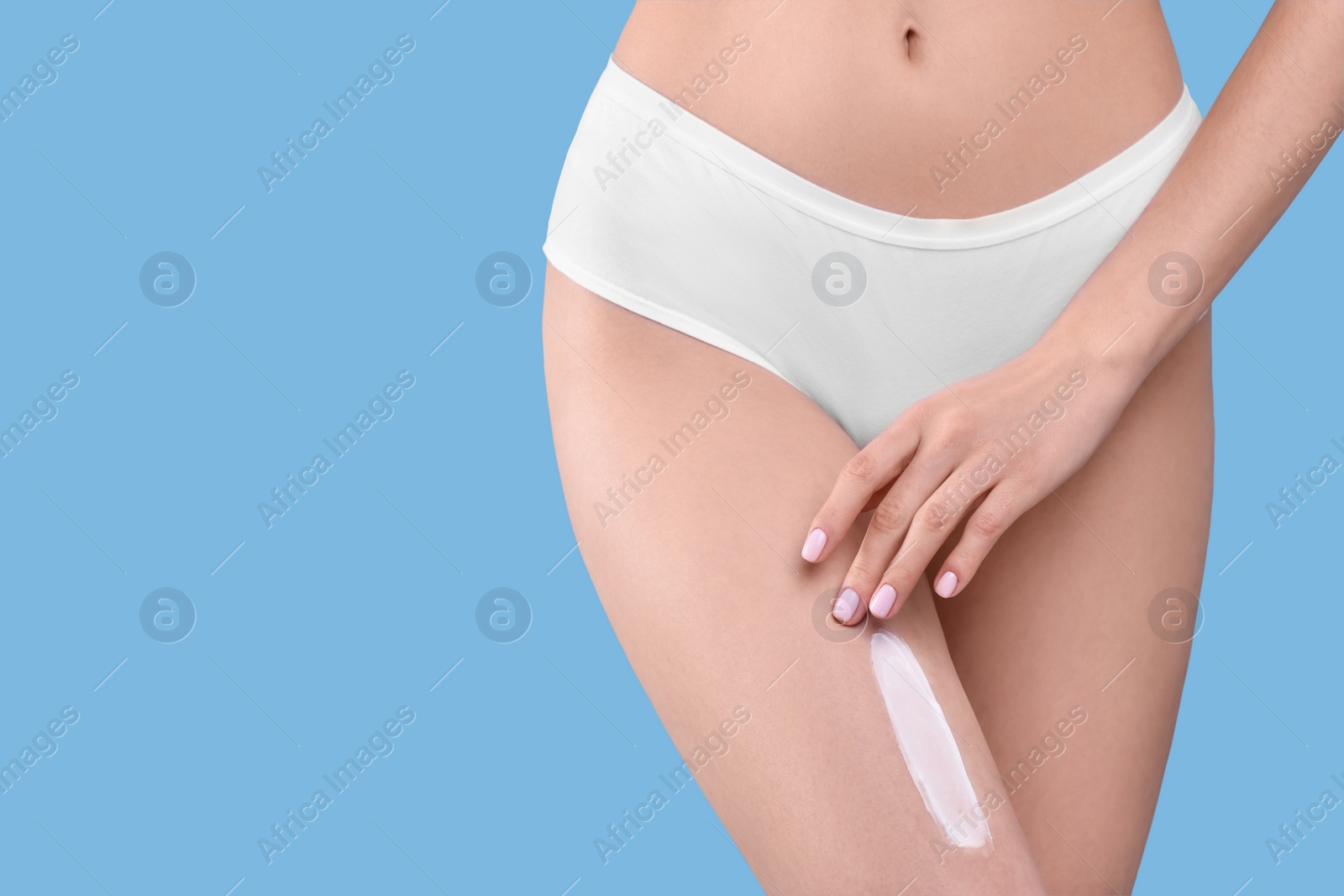 Photo of Woman with smear of body cream on her leg against light blue background, closeup. Space for text