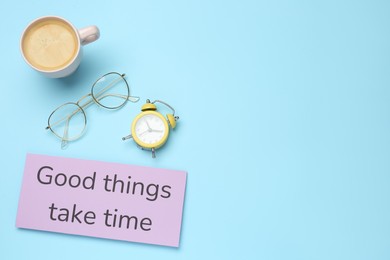 Photo of Note with motivational quote Good things take time, alarm clock, cup of coffee and glasses on light blue background, flat lay. Space for text