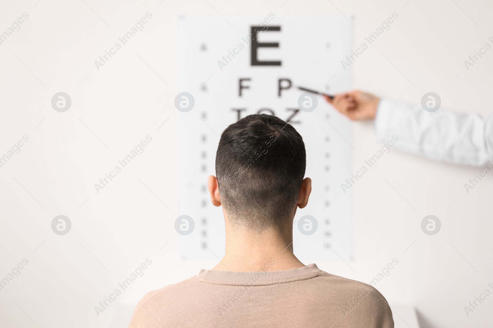 Photo of Ophthalmologist testing young man's vision in clinic, back view