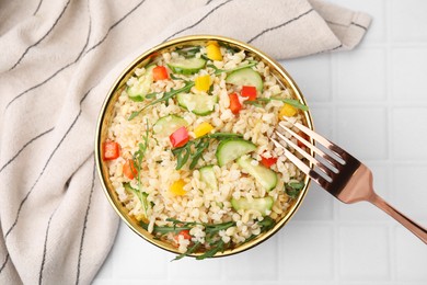 Photo of Cooked bulgur with vegetables in bowl on white tiled table, top view