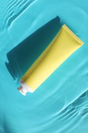 Tube with moisturizing cream in water on light blue background, top view