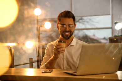 Photo of Man with cup of coffee working on laptop at table in office