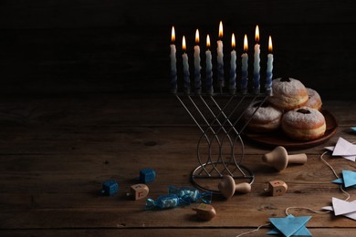 Photo of Hanukkah celebration. Menorah with burning candles, dreidels and donuts on wooden table, space for text