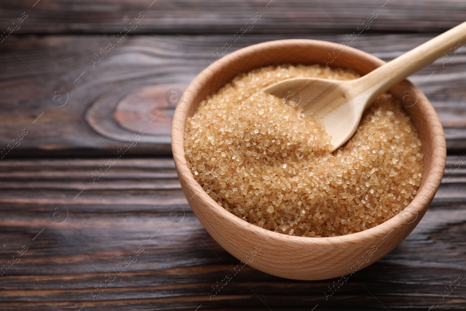 Photo of Bowl and spoon with brown sugar on wooden table, closeup. Space for text