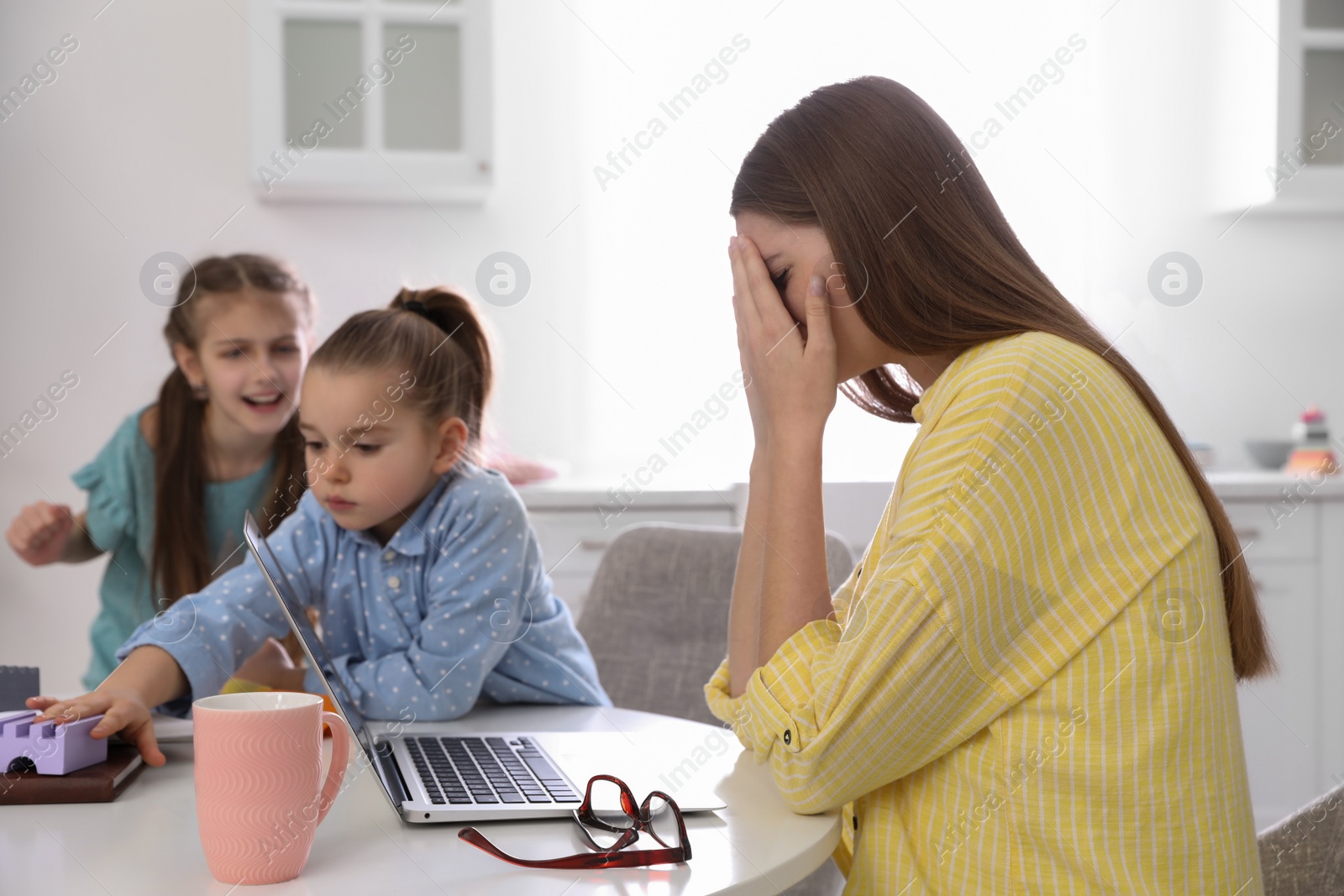 Photo of Children disturbing stressed woman in kitchen. Working from home during quarantine