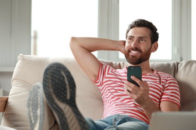 Photo of Handsome man using smartphone on sofa at home