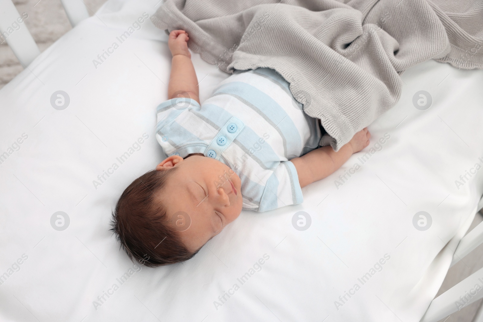 Photo of Cute newborn baby sleeping under blanket in crib. Bedtime