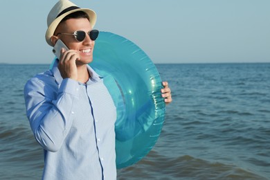 Photo of Happy man with inflatable ring talking by mobile phone near sea on beach. Business trip