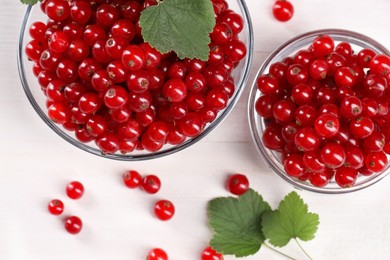 Photo of Many ripe red currants and leaves on white wooden table, flat lay