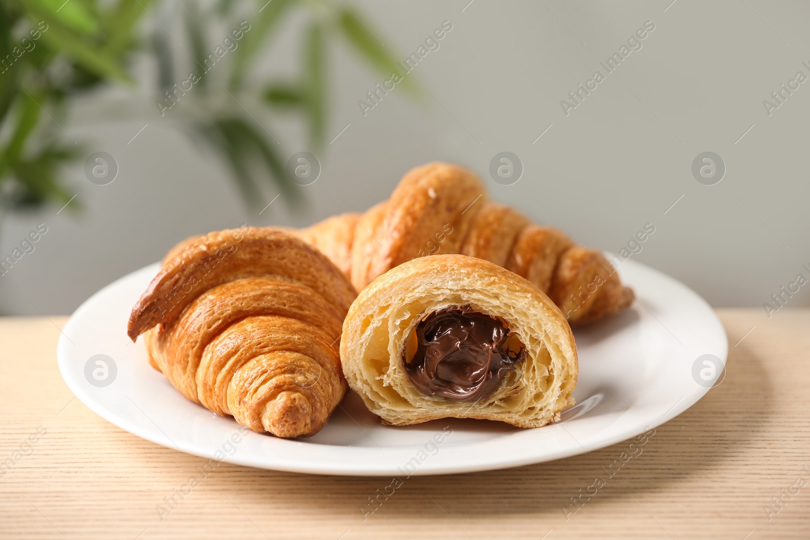 Photo of Plate of fresh croissants with chocolate stuffing on wooden table indoors, closeup. French pastry