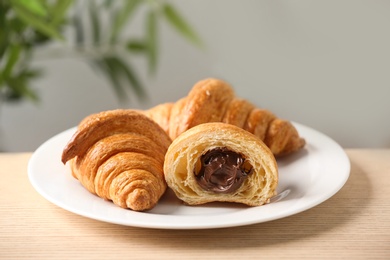 Plate of fresh croissants with chocolate stuffing on wooden table indoors, closeup. French pastry