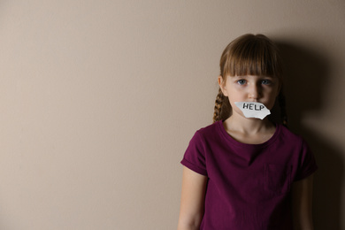 Sad little girl with sign HELP on beige background, space for text. Child in danger