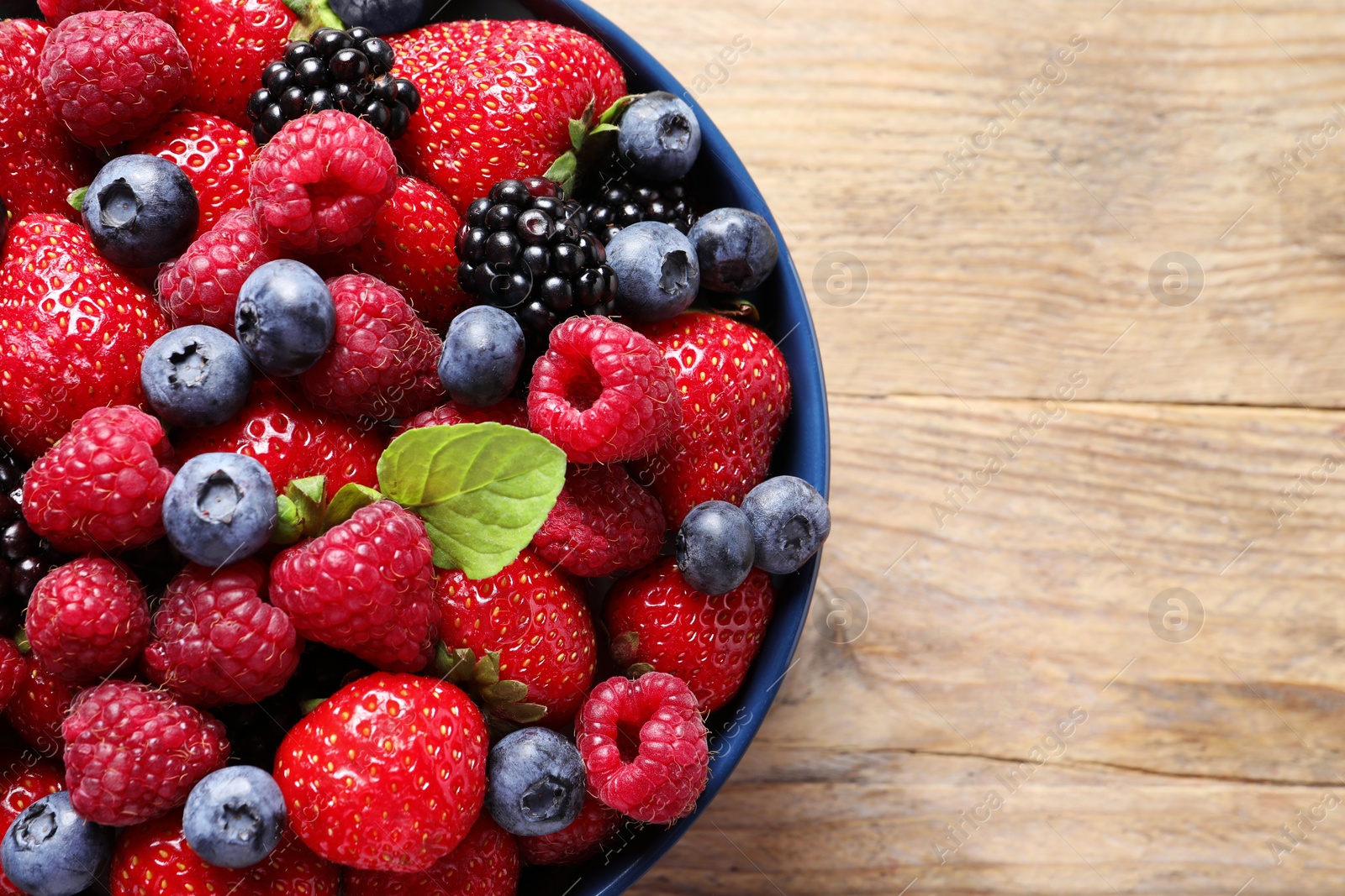 Photo of Different fresh ripe berries in bowl on wooden table, top view. Space for text