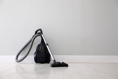 Photo of Modern vacuum cleaner near light wall indoors, space for text