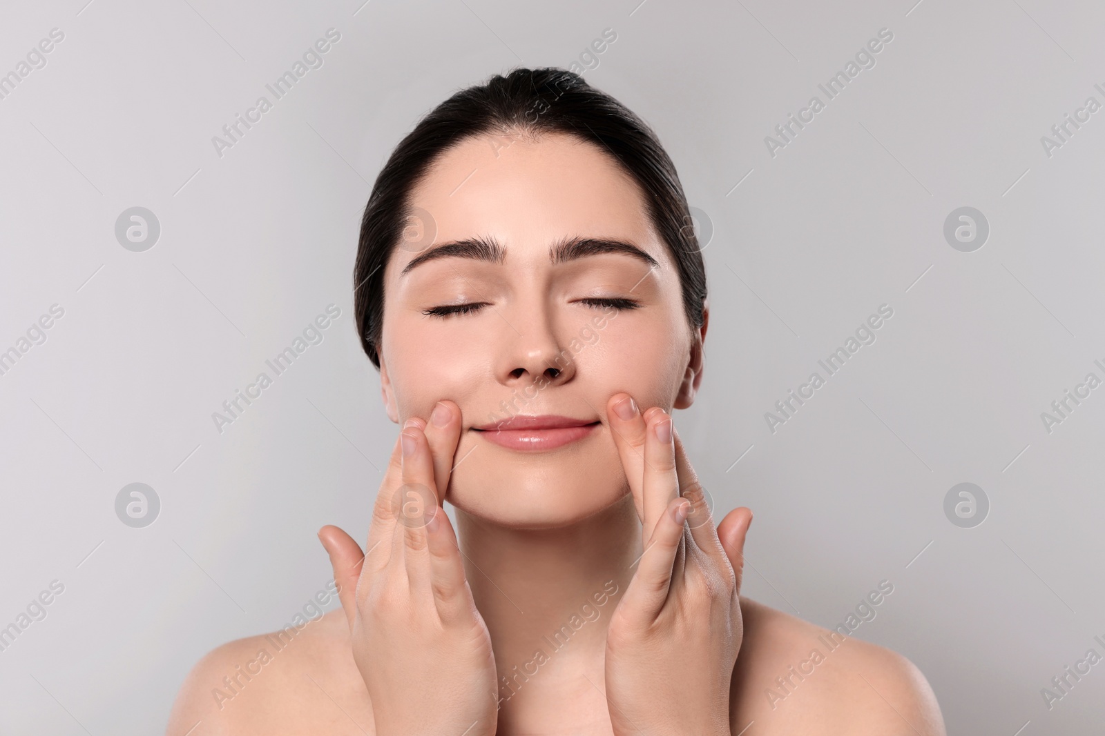 Photo of Young woman massaging her face on grey background