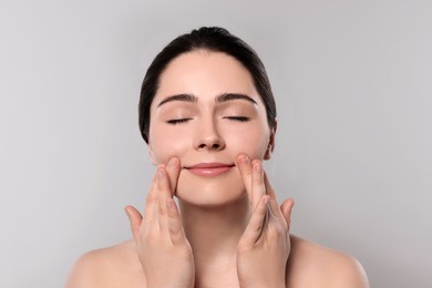 Young woman massaging her face on grey background