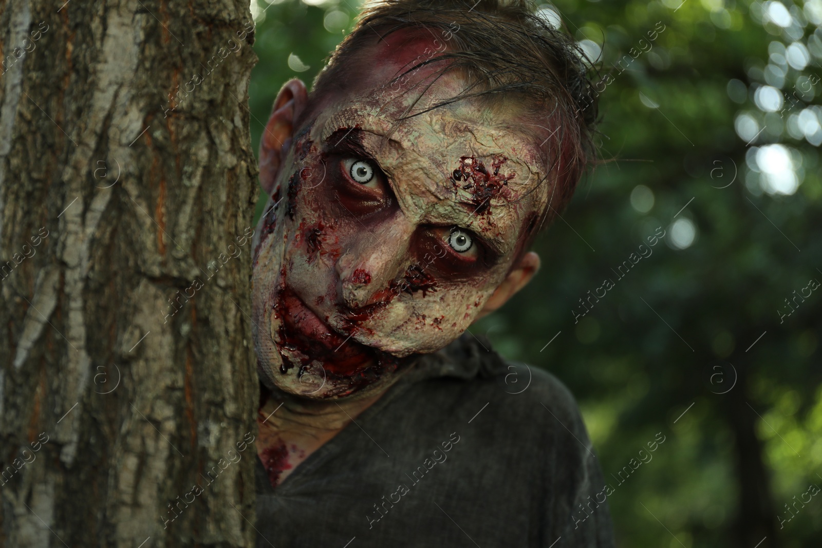 Photo of Scary zombie near tree outdoors. Halloween monster