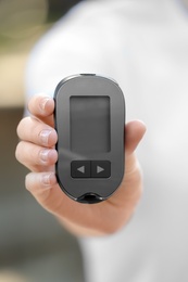 Photo of Woman holding digital glucometer on blurred background. Diabetes control