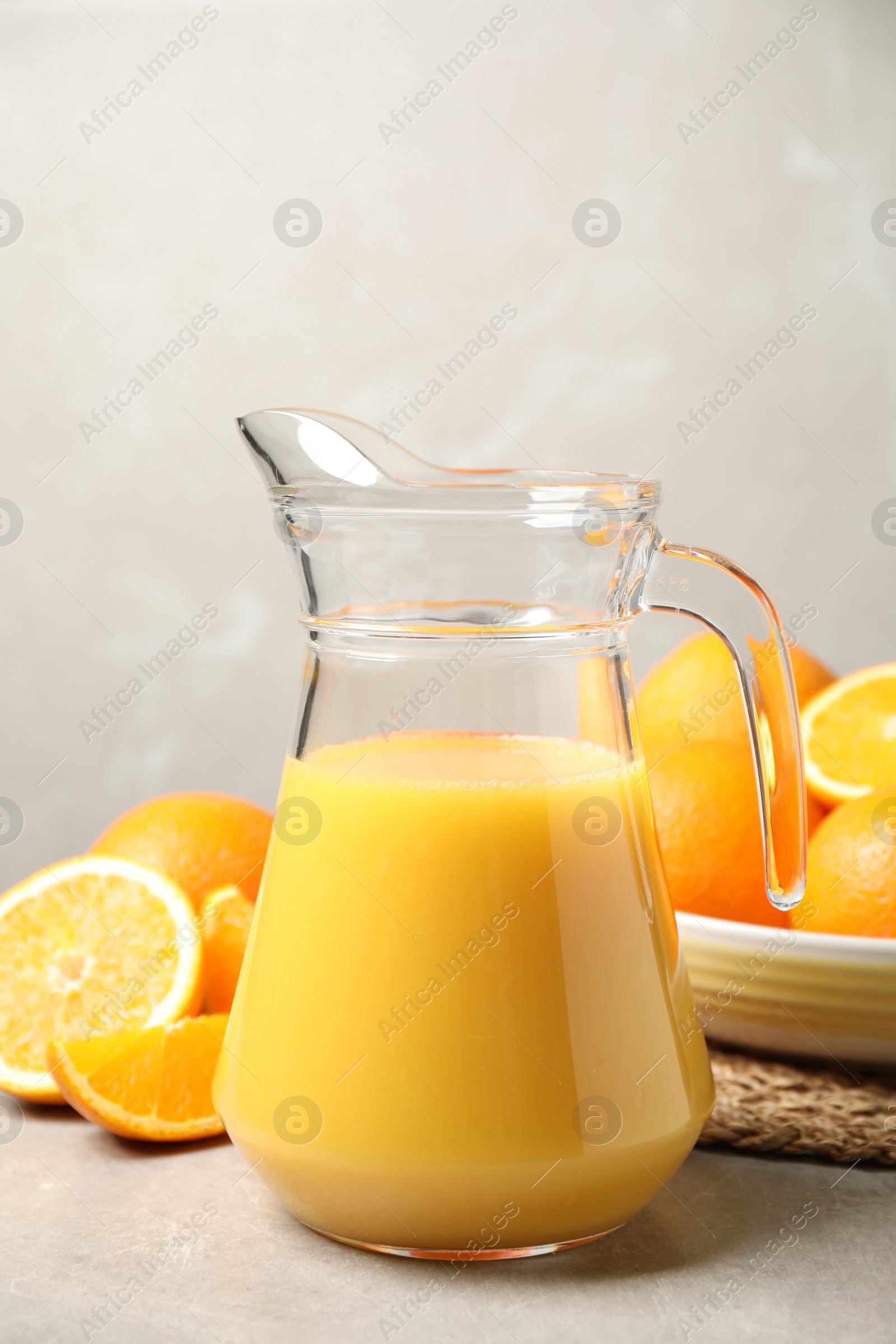 Photo of Jug of orange juice and fresh fruits on light grey table