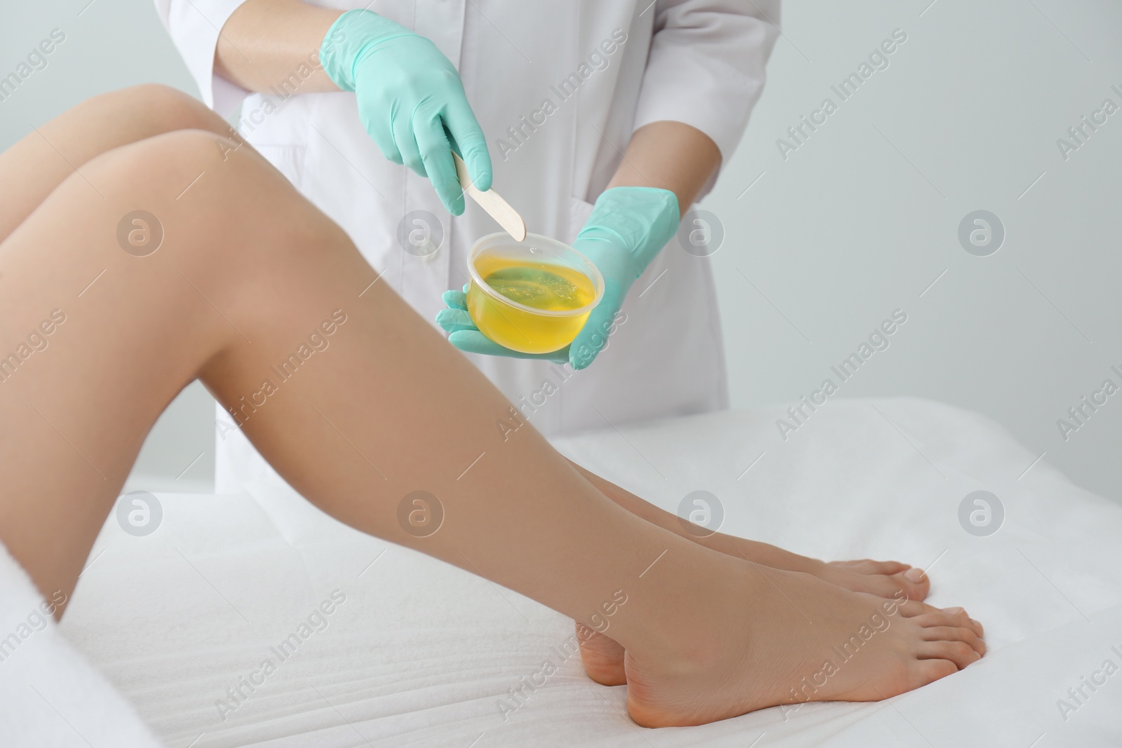 Photo of Woman getting wax epilation of legs in salon, closeup