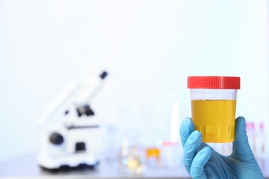 Photo of Laboratory assistant holding urine sample in container indoors, closeup with space for text. Medical analysis
