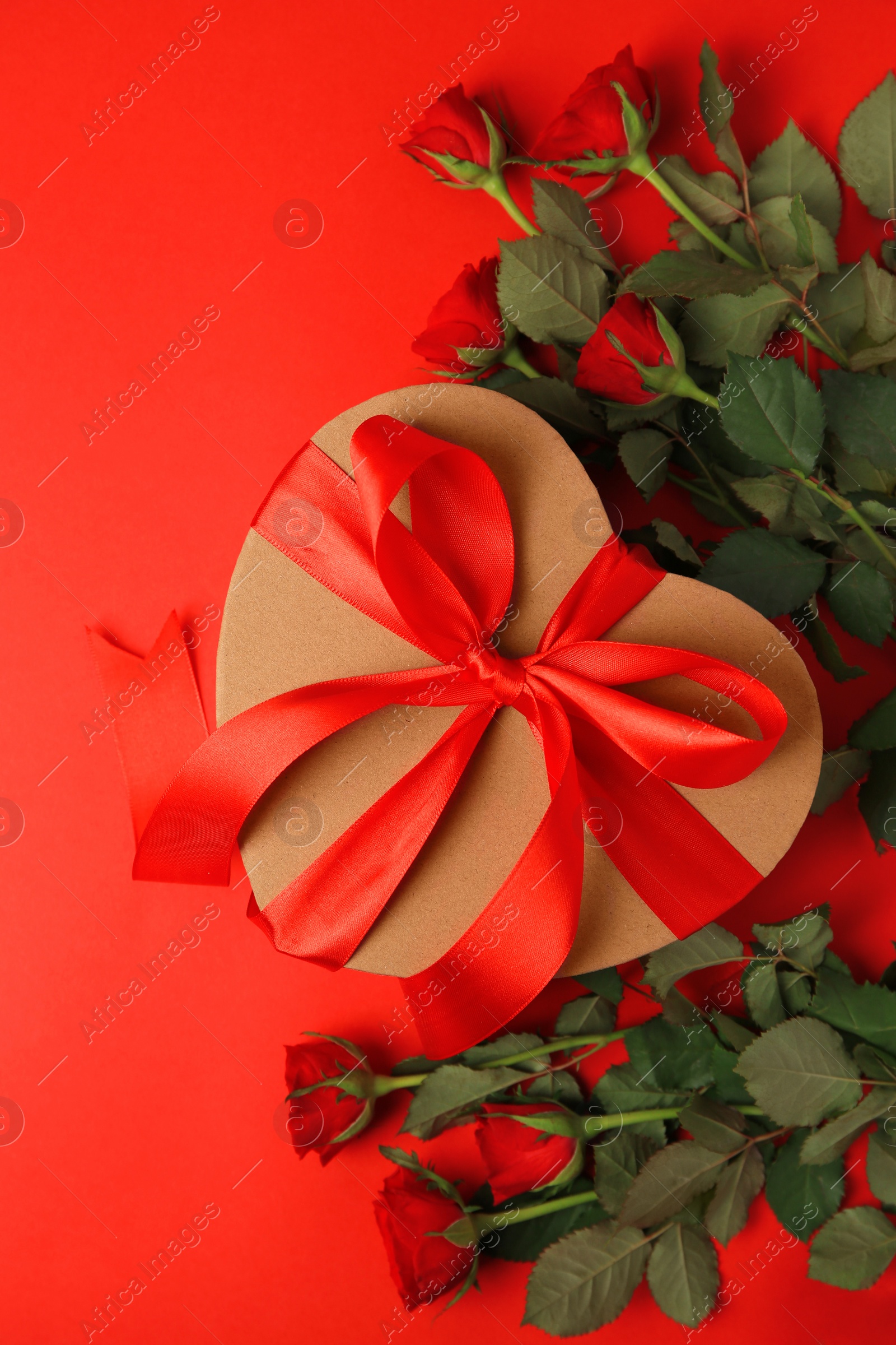 Photo of Heart shaped gift box with bow and beautiful roses on red background, flat lay