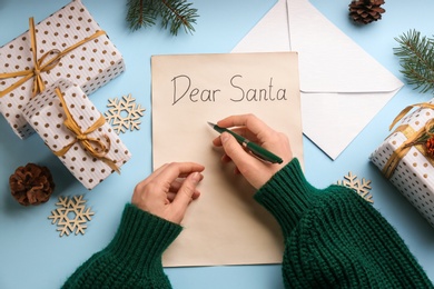 Top view of woman writing letter to Santa at light blue table, closeup