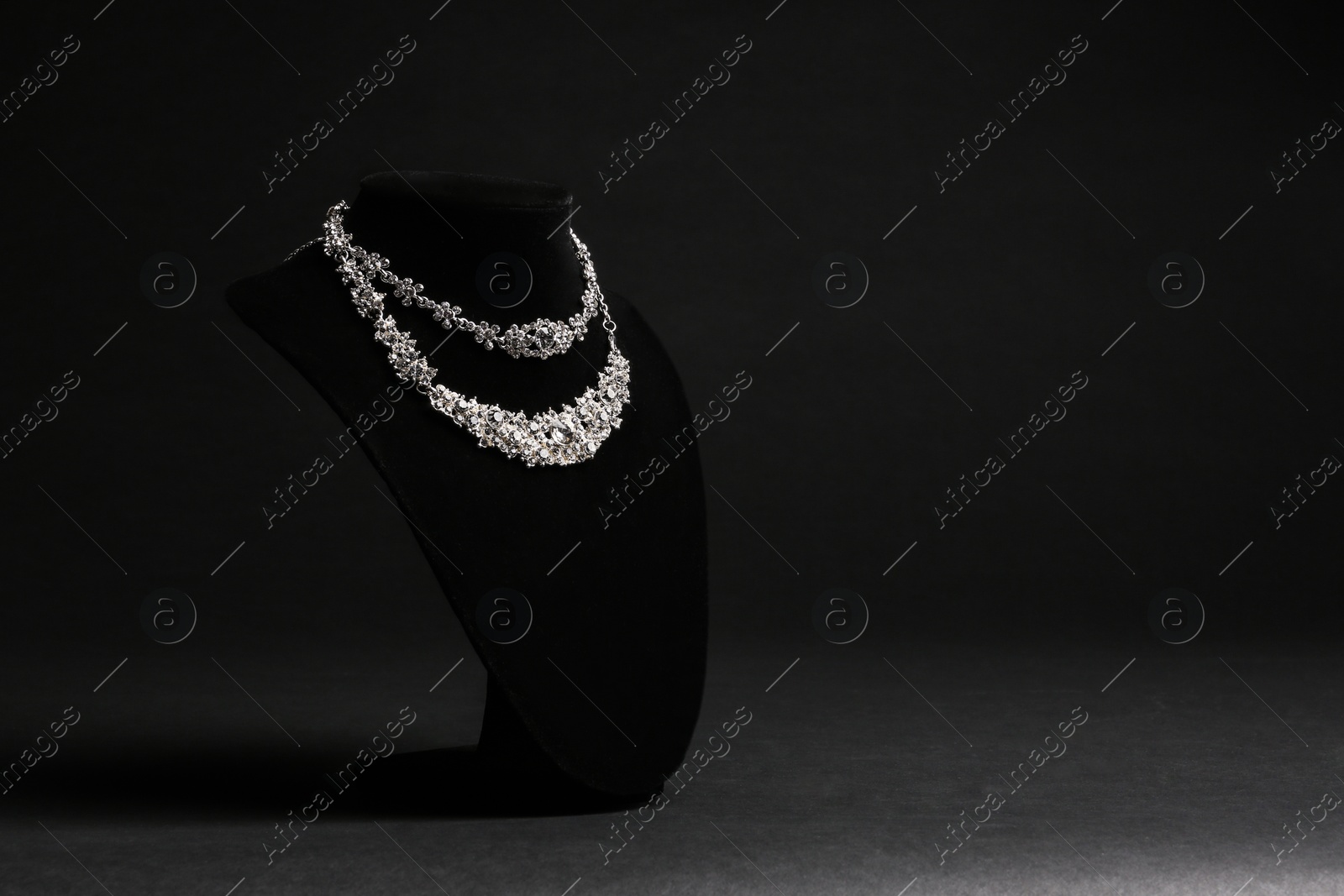 Photo of Elegant necklaces on stand against black background, space for text. Luxury jewelry