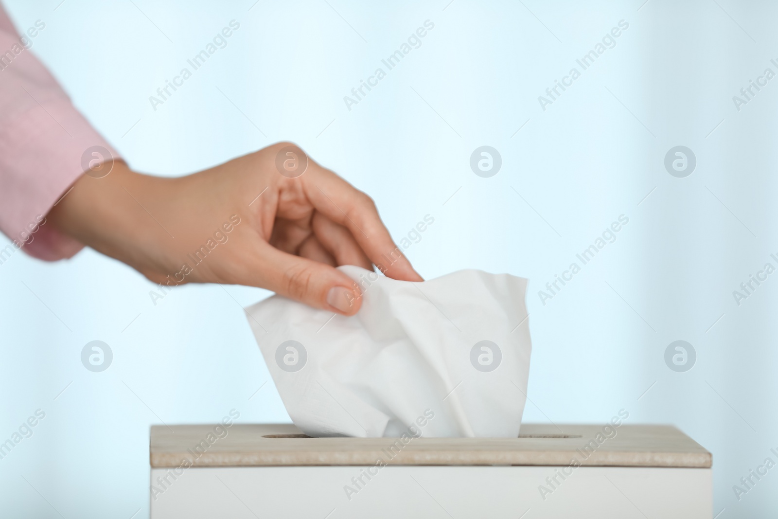 Photo of Woman taking paper tissue from holder on light background, closeup