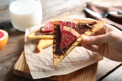 Woman eating toast with grapefruit, chocolate paste and chia seeds at table, closeup