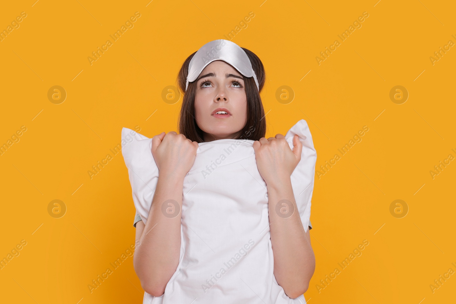 Photo of Unhappy young woman with sleep mask and pillow on yellow background. Insomnia problem